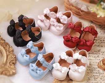 Può includere: Sei paia di scarpe in miniatura per bambole con fiocchi. Le scarpe sono di vari colori, tra cui rosa, rosso, nero, bianco e blu.