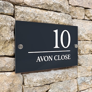 Può includere: Cartello nero per numeri civici con lettere bianche. Il numero 10 è visualizzato sopra il testo "Avon Close".