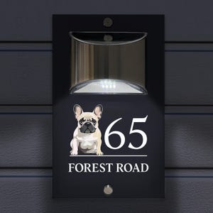 以下が含まれることがあります： 白いフレンチブルドッグのイラスト、数字の65、そして「FOREST ROAD」という文字が書かれた黒い家の番号札。この札にはソーラーライトが内蔵されています。