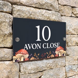 Peut inclure: Panneau de numéro de maison noir avec du texte blanc et des illustrations de champignons rouges. Le panneau indique "10 Avon Close".