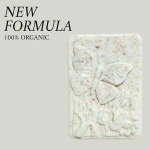May include: A rectangular bar of soap with a butterfly and floral design. The soap is off-white with a speckled texture. The words "NEW FORMULA" and "100% ORGANIC" are printed on the top left.