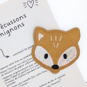 Può includere: Una toppa ricamata a forma di volpe marrone con dettagli bianchi e occhi neri. La toppa è su uno sfondo bianco con il testo "les écussons mignons" e "comment les poser".