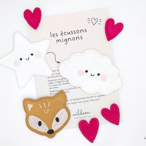 May include: Five embroidered iron-on patches: a white star, a white cloud, a brown fox, and two pink hearts. The patches have cute faces and are labeled "les écussons mignons".