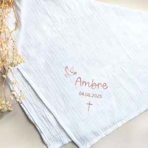Peut inclure: Tissu de mousseline blanc avec une colombe brodée en or rose, le nom "Ambre" et la date "04.06.2025". Une petite croix est également brodée sous la date.