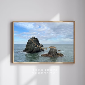 Puede incluir: Una impresión fotográfica digital enmarcada con dos grandes rocas en el océano conectadas por una cuerda. Las rocas son de color gris oscuro y el agua es de un azul-verdoso apagado. El cielo está nublado con parches azules.