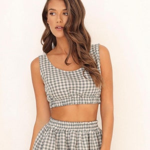 May include: A two-piece outfit featuring a white and blue gingham crop top and a matching midi skirt. The skirt has a gathered waist and a flowy silhouette.