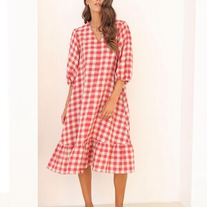 Può includere: Un abito midi a quadri vichy rosso e bianco con scollo a V e maniche 3/4. L'abito ha un orlo a balze e una vestibilità rilassata.