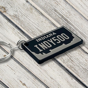 Puede incluir: Llavero negro y plateado con forma de matrícula de Indiana con el texto "INDY 500".