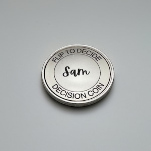 Może przedstawiać: Srebrna moneta decyzyjna z napisem "Flip to Decide" i "Decision Coin" wokół krawędzi. W środku monety znajduje się imię "Sam" napisane kursywą.