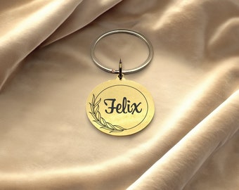 May include: Gold-coloured metal keychain with a round tag featuring a wreath design and the name "Felix" in black lettering.