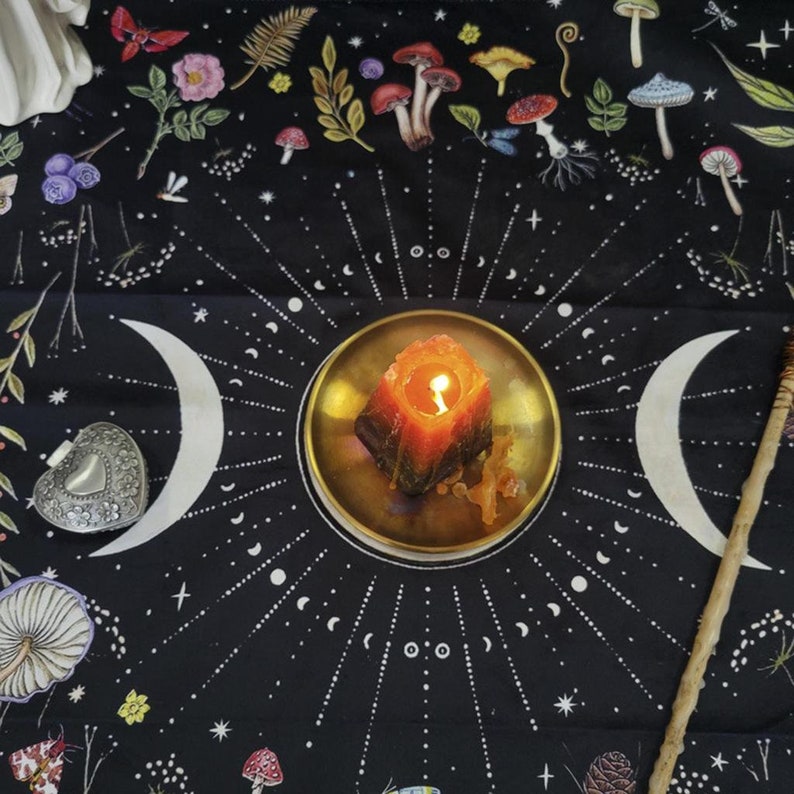 Peut inclure: Une tapisserie noire avec un motif de lune et d'&eacute;toiles blanches. Une bougie allum&eacute;e est plac&eacute;e dans un plat dor&eacute; au centre de la tapisserie. La tapisserie est entour&eacute;e d'une vari&eacute;t&eacute; de petits champignons color&eacute;s.
