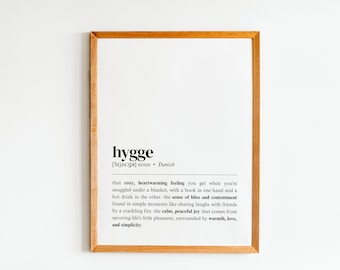 Könnte beinhalten: Ein gerahmter Druck mit weißem Hintergrund und schwarzem Text, der das dänische Wort "hygge" als ein gemütliches, herzerwärmendes Gefühl definiert. Der Text beschreibt das Gefühl als in einfachen Momenten zu finden, wie zum Beispiel beim Lachen mit Freunden am Kaminfeuer.