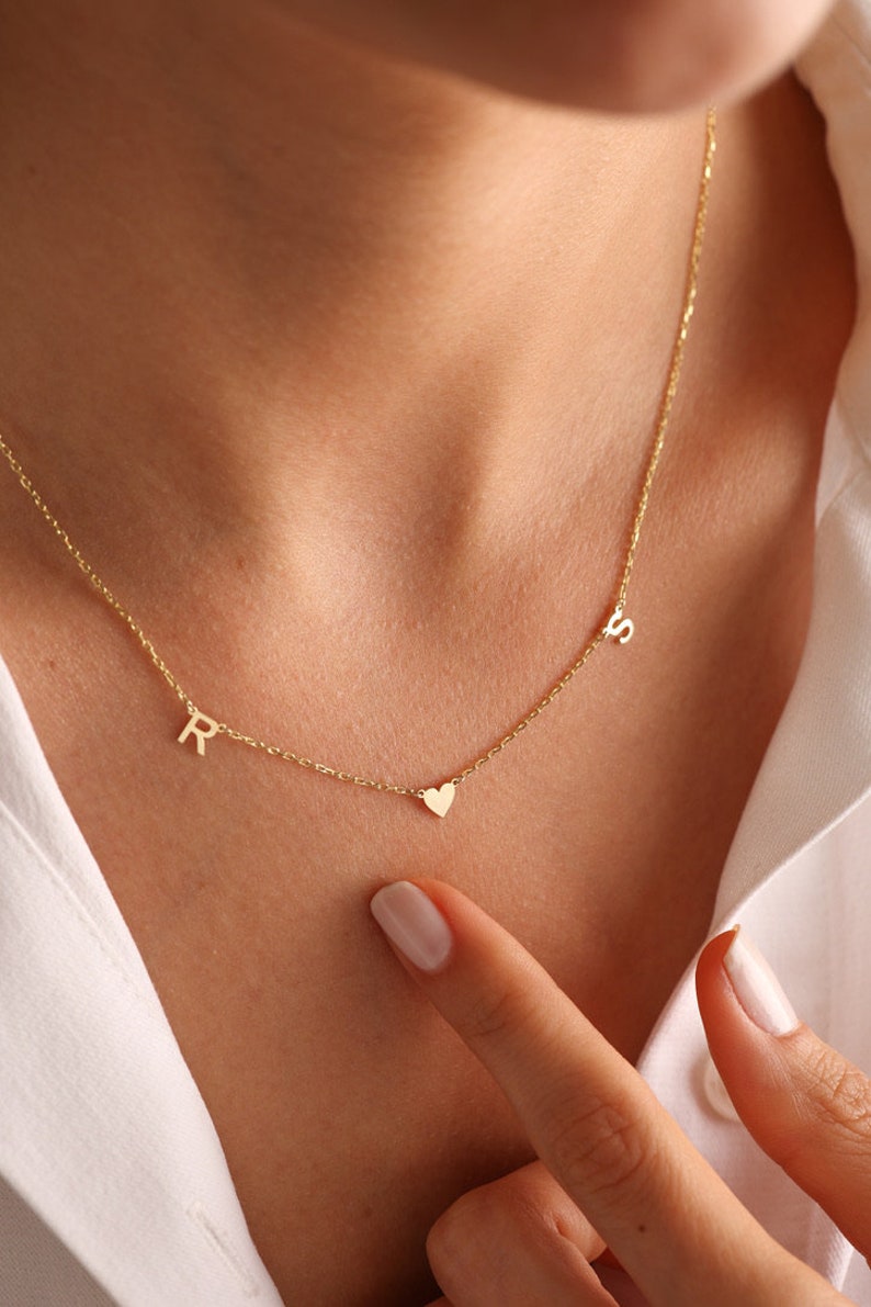 Puede incluir: Un collar de oro con un dije de coraz&oacute;n y dos dijes con iniciales. Las iniciales son "R" y "S".
