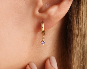 May include: Gold hoop earrings with a dangling purple gemstone.