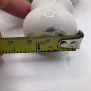 May include: White ceramic knob with a floral design. The knob is 5 cm in diameter.