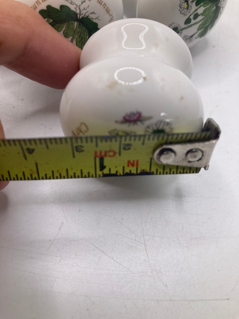 May include: White ceramic knob with a floral design. The knob is 5 cm in diameter.