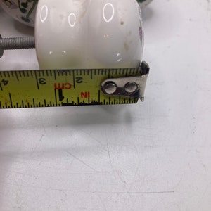 May include: White ceramic knob with a floral design and a screw. The knob is 5 cm in diameter.