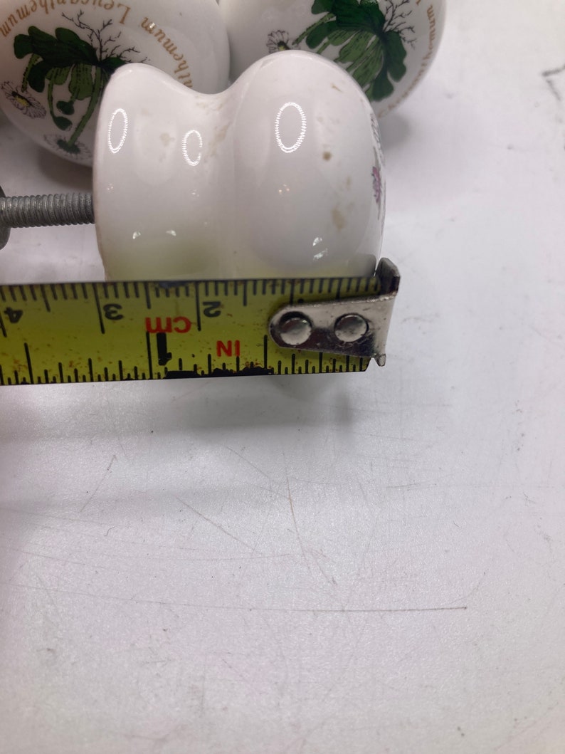May include: White ceramic knob with a floral design and a screw. The knob is 5 cm in diameter.