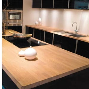 Puede incluir: Una encimera de cocina moderna hecha de madera clara con una placa de cocción de inducción negra y un fregadero negro. La encimera está delante de armarios negros.