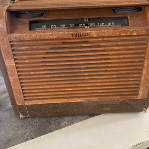 May include: A vintage wooden Philco radio with a brown wood cabinet and a black dial with white numbers. The radio has a metal grill on the front and a brown leatherette trim.