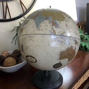 Może przedstawiać: Globus w stylu vintage z kremową powierzchnią, przedstawiający kontynenty i oceany w stonowanych odcieniach. Globus stoi na czarnej podstawie i posiada wzór róży wiatrów. Przedmiot dekoracyjny do domu lub biura.