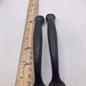 Könnte beinhalten: Zwei schwarze Metall-Schranktürgriffe mit strukturierter Oberfläche. Die Griffe sind etwa 18 cm lang.