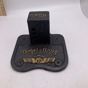 May include: A black cast iron base with a gold inscription that reads "Orgel-Gong" and a smaller gold inscription that reads "Wenzel". The base has a square black cast iron post attached to the top.