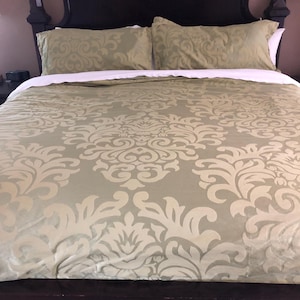 Pode incluir: Uma cama com cabeceira e estrutura castanho-escura. A cama é feita com um edredom verde claro e fronhas a condizer. O edredom e as fronhas têm um grande padrão floral creme ornamentado.