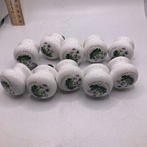 May include: Ten white ceramic cabinet knobs with a floral design. Each knob features a green and white illustration of a Chrysanthemum flower with the text "Chrysanthemum" written around the flower.