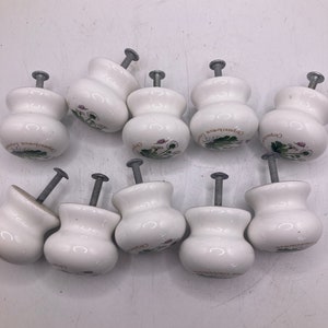 May include: Ten white ceramic cabinet knobs with a floral design and the text "Chrysanthemum" on each knob.