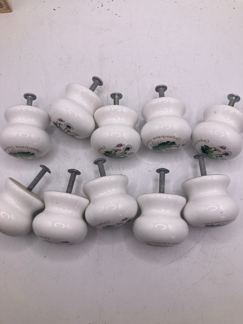 May include: Ten white ceramic cabinet knobs with a floral design and the text "Chrysanthemum" on each knob.