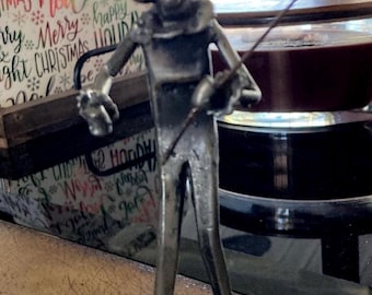 May include: A silver metal figurine of a jester holding a fishing rod. The jester is wearing a pointed hat and has a large, exaggerated nose.