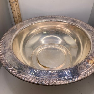 May include: A silver serving bowl with a decorative rim and a smaller bowl inside. The bowl is made of polished metal and has a reflective surface.