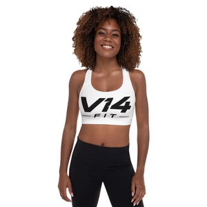 Puede incluir: Un sujetador deportivo blanco con espalda cruzada que presenta el texto negro en negrita V14 FIT impreso en la parte frontal del pecho. La prenda tiene un escote redondo y tirantes anchos para un ajuste seguro al hacer deporte.