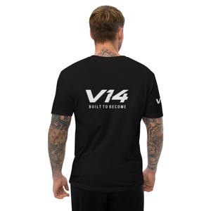 Puede incluir: Una camiseta negra de manga corta con el texto blanco V14 y la frase BUILT TO BECOME impresa en la espalda. Un logotipo V14 blanco más pequeño también es visible en la manga izquierda. La camiseta se muestra desde atrás en una persona.