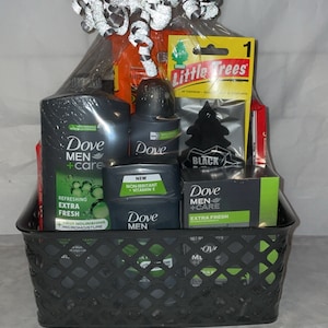 Op de afbeelding: Een zwarte draadmand gevuld met een cadeaupakket met Dove Men+Care douchegel, deodorant en body spray. De mand bevat ook een autoluchtverfrisser en een pak kauwgom.
