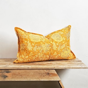 Pode incluir: Uma almofada de arremesso amarela mostarda com um padrão floral. A almofada está sentada em um banco de madeira rústico.