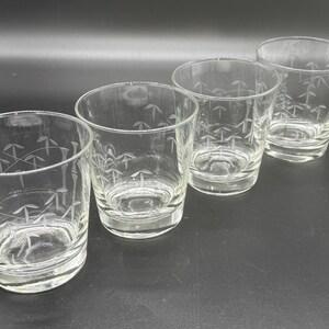 May include: Four clear glass tumblers with etched bamboo leaf designs. The glasses are arranged in a row, showcasing their simple, elegant shape. Ideal for serving beverages, these glasses add a touch of sophistication to any table setting.