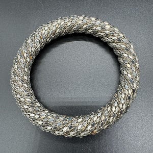 May include: A silver chain bracelet with a twisted design. The bracelet is made of small, linked metal pieces.