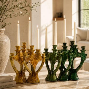 May include: A collection of six ceramic candelabras in mustard yellow and deep green, each featuring a sculptural, open-work design with multiple arms. Each candelabra holds a single white taper candle, creating a balanced display of light.