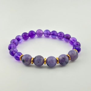 May include: A purple amethyst gemstone bracelet with gold accents. The bracelet is made with round beads and has a simple design.