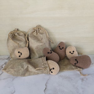 May include: A set of six crocheted potato toys with happy faces. The potatoes are in various shades of brown and beige. The potatoes are sitting on top of hessian bags.