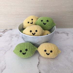 May include: A white bowl filled with crocheted lemon and lime shaped toys. The toys have smiling faces and are in various shades of yellow and green.