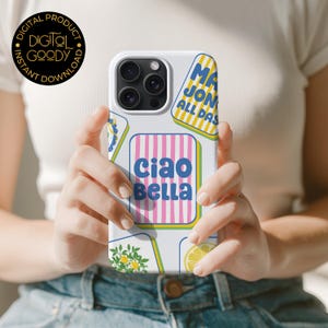 May include: White phone case with a colorful design featuring the words "Ciao Bella" in blue and pink, along with other text and illustrations. The case has a glossy finish and is held by a person.
