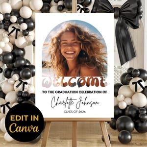 May include: A graduation celebration welcome sign featuring a smiling woman in a photo. The sign includes the text "WELCOME" and "TO THE GRADUATION CELEBRATION OF Charlotte Johnson CLASS OF 2026". The sign is on an easel.