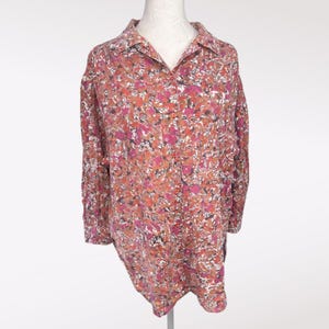 May include: A long-sleeved button-down shirt with a floral pattern in shades of pink, orange, and white. The shirt has a collared neckline and is displayed on a mannequin. The fabric appears to be lightweight.