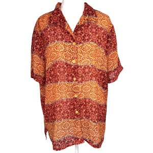 May include: A short-sleeved button-down shirt with a floral pattern in shades of red, gold, and orange. The shirt has a collared neckline and is buttoned up. The fabric appears to be lightweight and flowy.