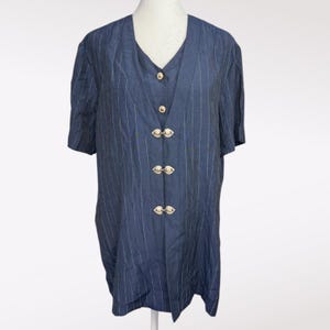 May include: A navy blue short-sleeved blouse with vertical white pinstripes. The blouse has a V-neck and is fastened with four decorative gold-colored clasps. The garment is displayed on a mannequin.