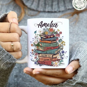 May include: White ceramic mug with a personalized name "Amelia" printed on it. The mug features a colorful illustration of a stack of books with flowers and butterflies.