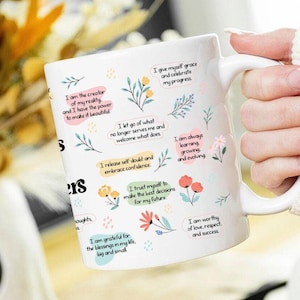 May include: White ceramic mug with inspirational affirmations and floral illustrations. The mug features phrases like "I am the creator of my reality" and "I am worthy of love, respect, and success."